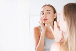 woman touching her nose while looking in the mirror